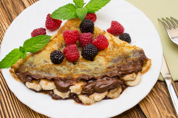 Homemade crepes served with chocolate cream, Banana, fresh blueberries, raspberries on a wooden background, pancakes
