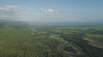 Aerial view river passing through farmlands and rice terraces. Philippines, Luzon. Tropical landscape with agricultural land near mountains and river flowing into sea.