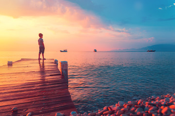 Silhouette of a child at sunset or sunrise at the sea in Greece or ocean on a beach in summer during vacation. Freedom, hope and travel destination concept when day meets night