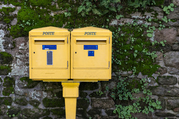 Two French letterboxes, with the word "post" written on them, against a stone wall covered with vegetation