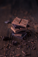 Column of dark or bitter or milk chocolate on a wood background.