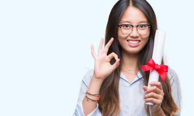 Young asian woman holding degree over isolated background doing ok sign with fingers, excellent symbol