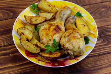 Baked chicken drumsticks with potatoes in a plate on wooden table