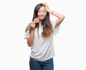 Fototapeta premium Young asian woman eating chocolate chip cookie over isolated background stressed with hand on head, shocked with shame and surprise face, angry and frustrated. Fear and upset for mistake.