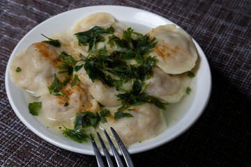 A plate of dumplings with greens and seasoning is on a napkin on the table next to the dough.