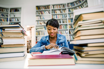 Pretty teenage black african college student girl studying and reading a book in college library