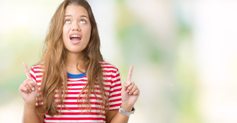 Young beautiful brunette woman wearing stripes t-shirt over isolated background amazed and surprised looking up and pointing with fingers and raised arms.
