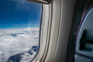 Looking outside from a commercial plane window. Outside is a sunny day with clouds. Inside the front seat can be seen.