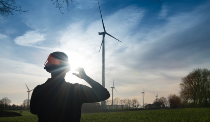 Man infront of a wind farm uses noise protector to reduce the noise of the wind turbine