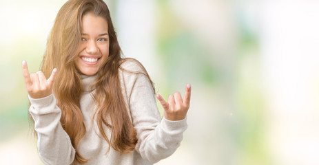 Young beautiful brunette woman wearing turtleneck sweater over isolated background shouting with crazy expression doing rock symbol with hands up. Music star. Heavy concept.