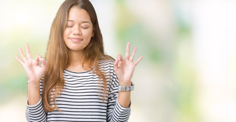 Young beautiful brunette woman wearing stripes sweater over isolated background relax and smiling with eyes closed doing meditation gesture with fingers. Yoga concept.