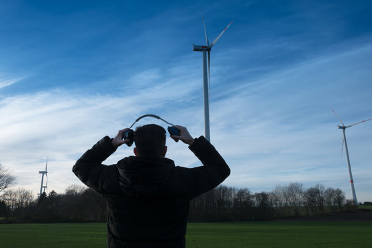 Man infront of a wind farm uses noise protector to reduce the noise of the wind turbine