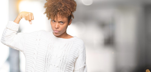 Beautiful young african american woman wearing winter sweater over isolated background Strong person showing arm muscle, confident and proud of power