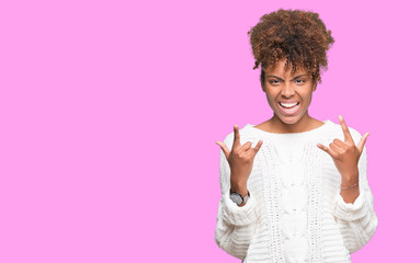 Beautiful young african american woman wearing winter sweater over isolated background shouting with crazy expression doing rock symbol with hands up. Music star. Heavy concept.