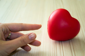 Hand is streching to red heart on white wooden table. Love concept. Happy Valentine's Day.