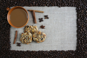 A cup of coffee surrounded by coffee beans, next to cinnamon and biscuits with nuts and raisins