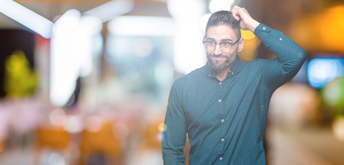 Young handsome business man wearing glasses over isolated background confuse and wonder about question. Uncertain with doubt, thinking with hand on head. Pensive concept.