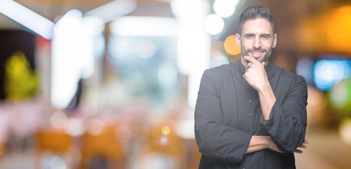 Young Christian priest over isolated background looking confident at the camera with smile with crossed arms and hand raised on chin. Thinking positive.