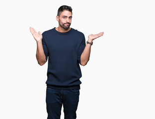 Young handsome man wearing sweater over isolated background clueless and confused expression with arms and hands raised. Doubt concept.