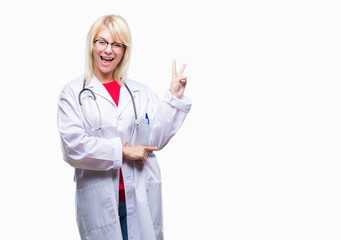 Young beautiful blonde doctor woman wearing medical uniform over isolated background smiling with happy face winking at the camera doing victory sign. Number two.