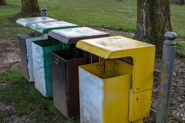 Fototapeta na wymiar Waste separation with four differently coloured waste bins on a meadow