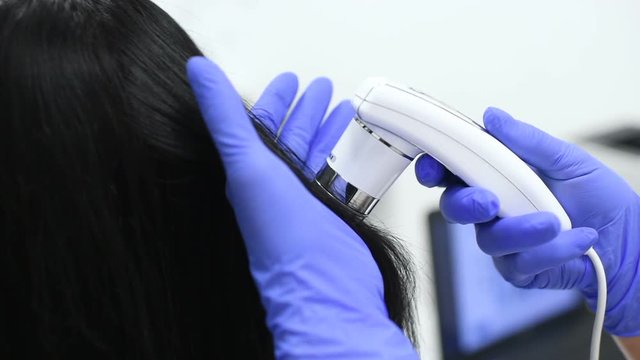 doctor dermatologist diagnoses the structure of the hair of a young pretty girl with a special tool - a trichoscope. Trichology, trichogram