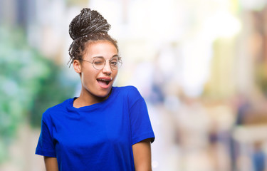 Young braided hair african american girl wearing glasses over isolated background winking looking at the camera with sexy expression, cheerful and happy face.