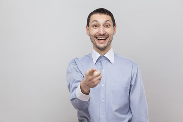 Is that was you? Amazed handsome bristle businessman in classic blue shirt standing, pointing and looking at camera with surprised face. indoor studio shot, isolated on grey background copyspace.