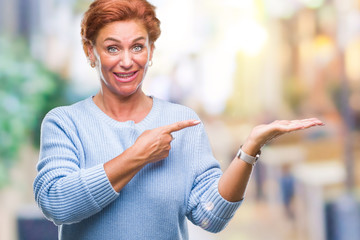 Atrractive senior caucasian redhead woman over isolated background amazed and smiling to the camera while presenting with hand and pointing with finger.