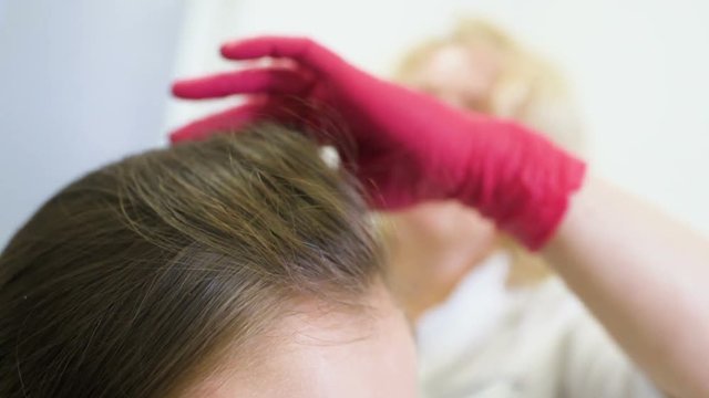 doctor dermatologist diagnoses the structure of the hair of a young pretty girl with a special tool - a trichoscope. Trichology, trichogram