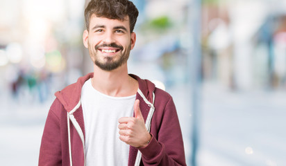 Young handsome man over isolated background doing happy thumbs up gesture with hand. Approving expression looking at the camera showing success.