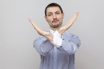There is no way. Portrait of handsome bristle businessman in classic light blue shirt standing, looking at camera with rejection block X sign. indoor studio shot, isolated on grey background copyspace
