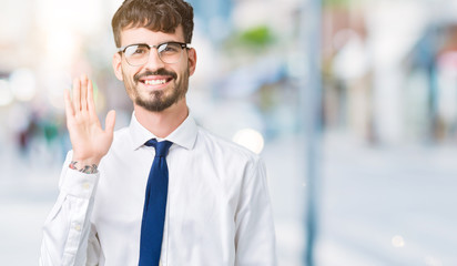 Young handsome business man wearing glasses over isolated background Waiving saying hello happy and...