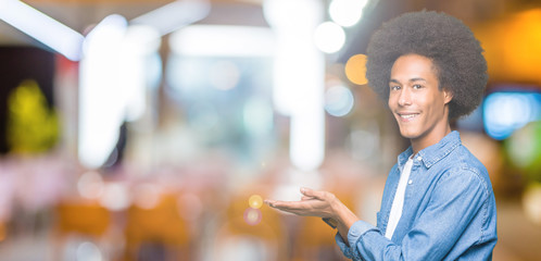 Young african american man with afro hair Pointing to the side with hand and open palm, presenting ad smiling happy and confident