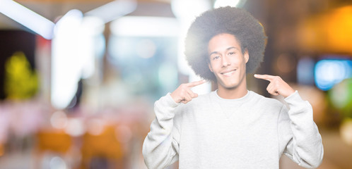 Young african american man with afro hair wearing sporty sweatshirt smiling confident showing and pointing with fingers teeth and mouth. Health concept.