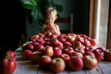Girl with fresh red apples on table at home