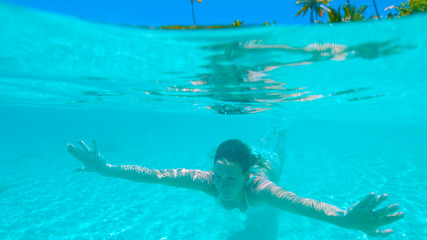 HALF IN HALF OUT: Carefree girl on vacation diving in the tranquil glassy ocean.