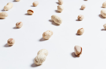 Various nuts: pistachio and shell peanuts repetition on white background as pattern, shallow depth of field.