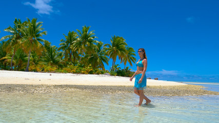Fototapeta na wymiar Young woman in bikini walking in the shallow ocean water and along sandy beach.