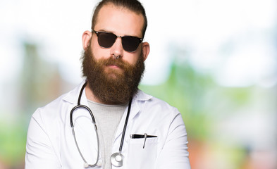 Young blond doctor man with beard wearing sunglasses skeptic and nervous, disapproving expression on face with crossed arms. Negative person.