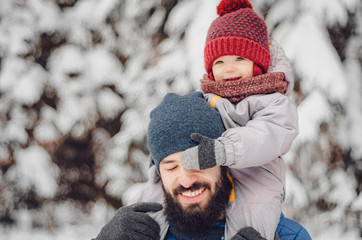 Portrait of a happy man piggybacking his cheerful son or daughter. father and baby on winter holidays walking in a snowy park.