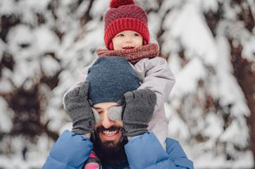 Portrait of a happy man piggybacking his cheerful son or daughter. father and baby on winter holidays walking in a snowy park.