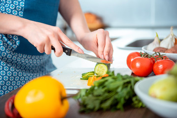 the young nice girl in a blue dress and an apron in kitchen cuts vegetables