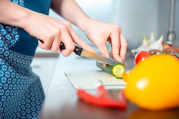 the young nice girl in a blue dress and an apron in kitchen cuts vegetables