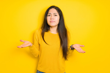 Beautiful brunette woman over yellow isolated background clueless and confused expression with arms and hands raised. Doubt concept.