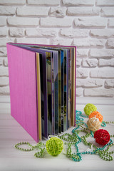 Vertical photo. Nice purple book staying on white table near colored rattan balls and glowing beads on brick wall background