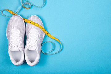 White sport shoes (sneakers) with measuring tape on blue background.