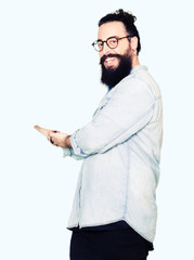 Young hipster man with long hair and beard wearing glasses Inviting to enter smiling natural with open hand