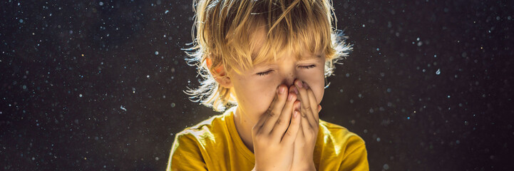 Allergy to dust. Boy sneezes because he is allergic to dust. Dust flies in the air backlit by light...