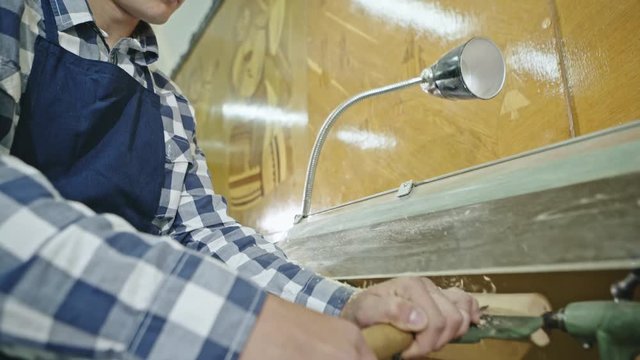 A young man manually lathing a piece of timber with a chisel in a workshop